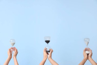 Mavi arka planda kum saati tutan kadın eller.