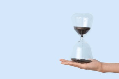 Mavi arka planda kum saati tutan kadın.