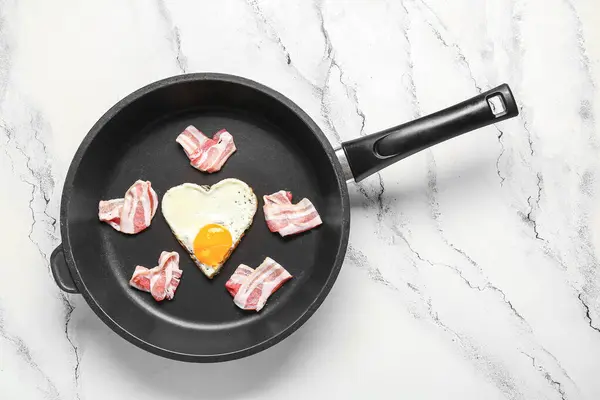 Frying pan with hearts made of tasty bacon and fried egg on light background