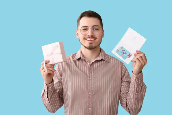 Schöner Mann Mit Geschenkkarte Und Geschenk Auf Blauem Hintergrund — Stockfoto