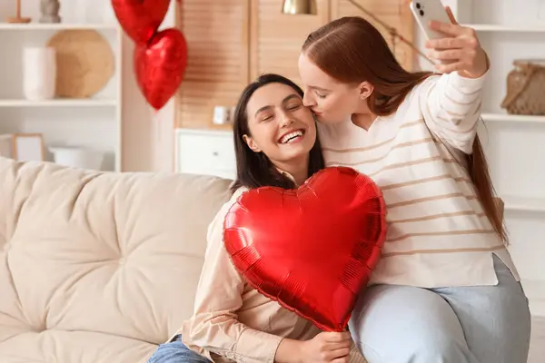 Kalp şeklinde balonları olan genç lezbiyen çift Sevgililer Günü 'nde evde selfie çekiyorlar.