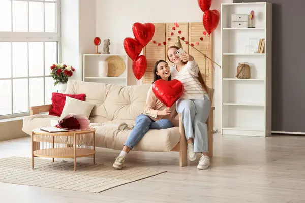 Kalp şeklinde balonları olan genç lezbiyen çift Sevgililer Günü 'nde evde selfie çekiyorlar.