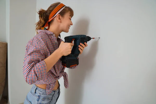 Young woman drilling wall during repair in room