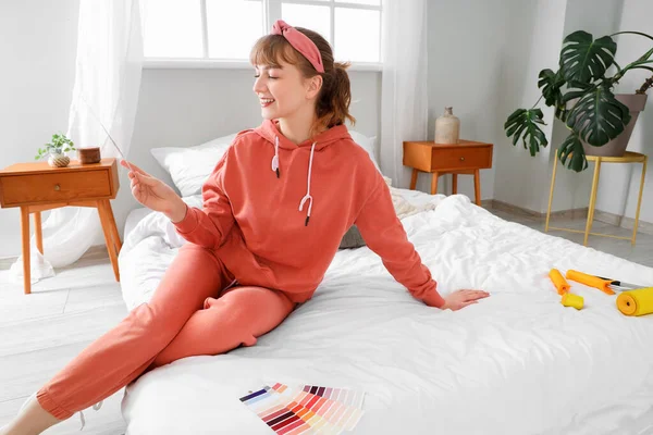Young woman with paint color palette sitting during repair in bedroom
