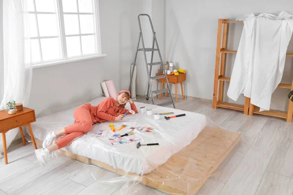 Young woman with paint tools lying during repair in bedroom