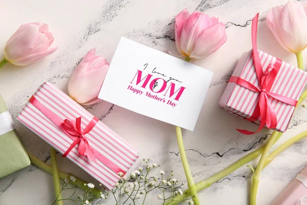 Mutlu Anneler Günü yazılı kart, hediye kutuları ve arka planda güzel çiçekler