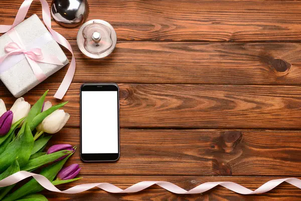 Modern cep telefonlu kompozisyon, güzel lale çiçekleri ve ahşap arka planda hediye kutusu.
