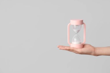 Gri arka planda kum saati tutan kadın.