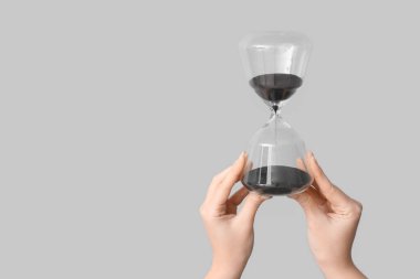 Gri arka planda kum saati tutan kadın eller.