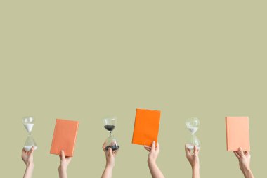 Kum saati tutan kadın eller ve yeşil arkaplan üzerine kitaplar