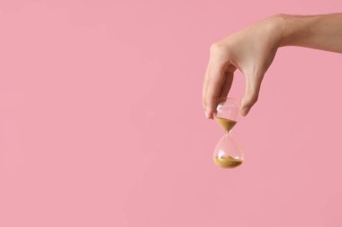 Pembe arka planda kum saati tutan kadın.