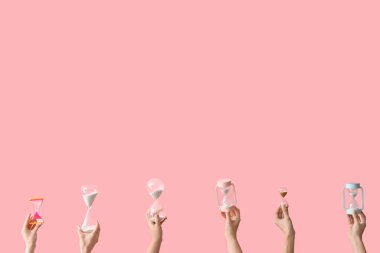 Pembe arka planda kum saati tutan kadın eller.