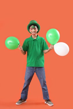 Yüzü boyalı, cüce şapkası ve turuncu arka planda balonları olan komik çocuk. Aziz Patrick Günü kutlaması