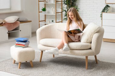 Evdeki kanepede kitap okuyan küçük kız.