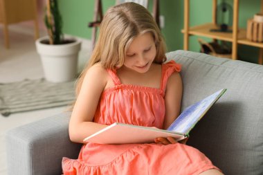 Evdeki kanepede kitap okuyan küçük kız.