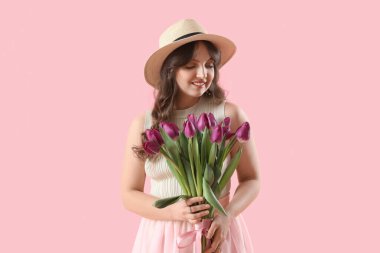 Pembe arka planda güzel mor lalelerle dolu buketi olan güzel genç bir kadın.