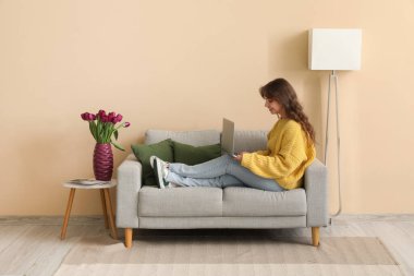 Evinde güzel lalelerle dolu vazo ve dizüstü bilgisayar kullanan güzel bir kadın.