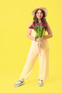 Sarı arka planda güzel mor lalelerle dolu buketi olan mutlu genç bir kadın.