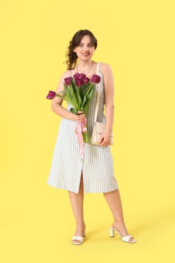 Sarı arka planda güzel mor lalelerle dolu buketi olan güzel genç bir kadın.