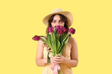 Sarı arka planda güzel mor lalelerle dolu buketi olan güzel genç bir kadın.