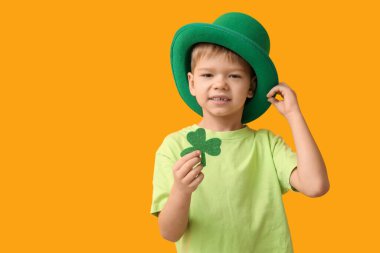 Sarı arka planda yonca olan leprikon şapkalı şirin bir çocuk. Aziz Patrick Günü kutlaması