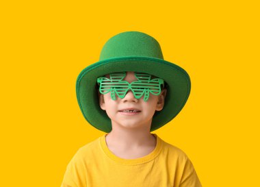 Leprikon şapkalı ve sarı arka planda yonca şeklinde dekoratif gözlüklü şirin bir çocuk. Aziz Patrick Günü kutlaması
