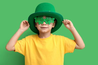 Leprikon şapkalı ve yeşil arka planda yonca şeklinde dekoratif gözlüklü şirin bir çocuk. Aziz Patrick Günü kutlaması