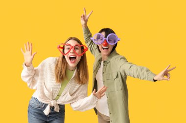 Sarı arka planda komik görünümlü güzel, genç, mutlu kadınlar. 1 Nisan şakası