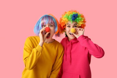 Pembe arka planda komik palyaço kılığına girmiş güzel, şok olmuş genç kadınlar. 1 Nisan şakası