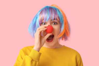 Pembe arka planda komik palyaço kılığına girmiş genç ve güzel bir kadın. 1 Nisan şakası