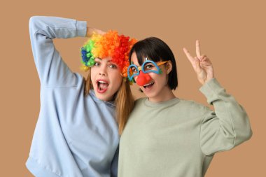 Kahverengi arka planda komik palyaço kılığına girmiş güzel, genç ve şok olmuş kadınlar. 1 Nisan şakası