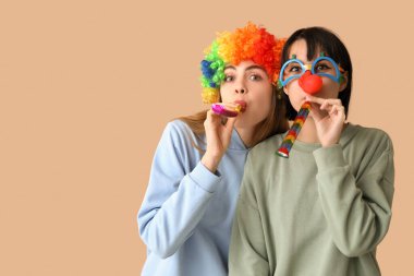 Kahverengi arka planda parti düdükleriyle komik palyaço kılığına girmiş güzel genç kadınlar. 1 Nisan şakası