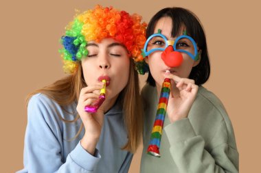 Kahverengi arka planda parti düdükleriyle komik palyaço kılığına girmiş güzel genç kadınlar. 1 Nisan şakası