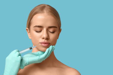 Genç bir kadın mavi arka planda dudaklarından enjeksiyon yaptırıyor.