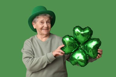 Yeşil arka planda yonca şeklinde hava balonu olan cüce şapkalı yaşlı kadın. Aziz Patrick Günü kutlaması