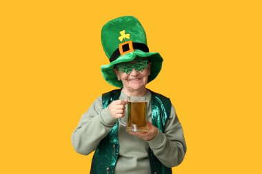 Leprikon şapkalı yaşlı kadın ve sarı arka planda bir bardak birayla dekoratif bardaklar. Aziz Patrick Günü kutlaması