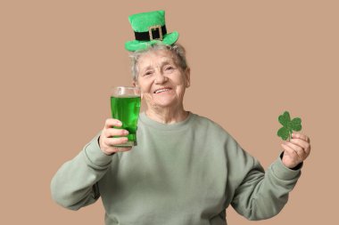 Kahverengi arka planda bir bardak bira ve yoncayla cüce şapkalı yaşlı kadın. Aziz Patrick Günü kutlaması
