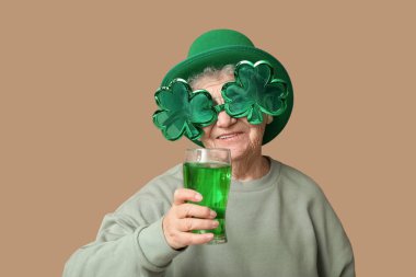 Kahverengi arka planda bir bardak birası olan cüce şapkalı ve dekoratif gözlüklü yaşlı kadın. Aziz Patrick Günü kutlaması