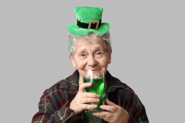 Gri arka planda bir bardak birayla cüce şapkalı yaşlı kadın. Aziz Patrick Günü kutlaması