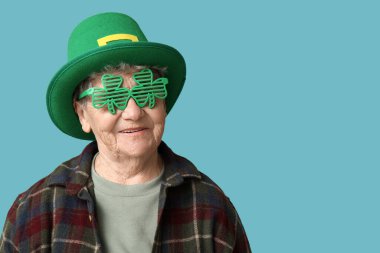 Leprikon şapkalı ve mavi arka planda yonca şeklinde dekoratif gözlüklü yaşlı kadın. Aziz Patrick Günü kutlaması