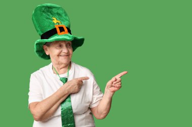 Yeşil arka plandaki bir şeyi işaret eden cüce şapkalı yaşlı kadın. Aziz Patrick Günü kutlaması