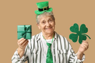 Kahverengi arka planda yonca ve hediye kutusu olan cüce şapkalı yaşlı kadın. Aziz Patrick Günü kutlaması