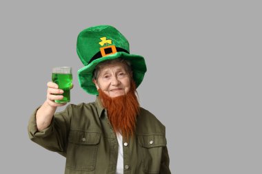 Kırmızı sakallı cüce şapkalı yaşlı kadın gri arka planda bir bardak bira tutuyor. Aziz Patrick Günü kutlaması