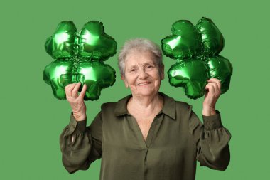 Yeşil arka planda yonca şeklinde balonları olan yaşlı bir kadın. Aziz Patrick Günü kutlaması