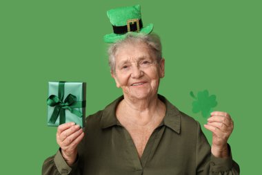 Yeşil arka planda yonca ve hediye kutusuyla cüce şapkalı yaşlı kadın. Aziz Patrick Günü kutlaması
