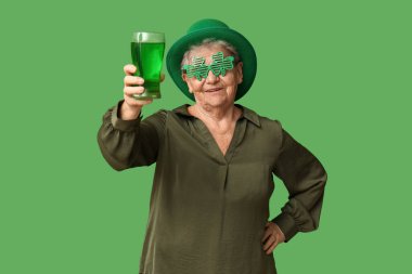 Yeşil arka planda bir bardak birası olan cüce şapkalı ve dekoratif gözlüklü yaşlı kadın. Aziz Patrick Günü kutlaması