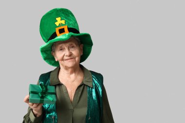 Gri arka planda hediye kutusu olan cüce şapkalı yaşlı kadın. Aziz Patrick Günü kutlaması