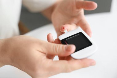 Glukometresi olan diyabetik kadın mutfakta kan şekerini ölçüyor, yakın plan.