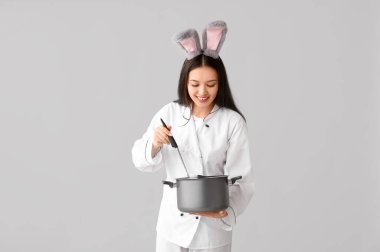 Tavşan kulaklı, hafif arka planda tenceresi olan Asyalı bir kadın şef. Paskalya kutlaması