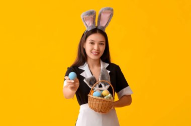 Sarı arka planda Paskalya yumurtaları olan tavşan kulaklı genç Asyalı oda hizmetçisi.